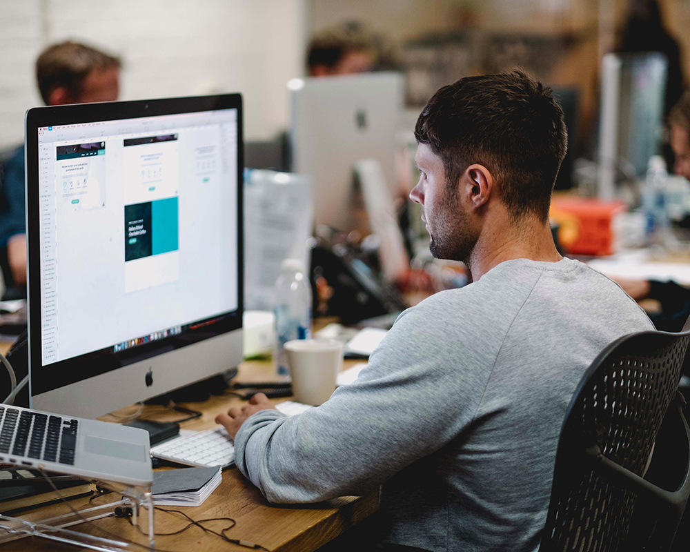 Man sitting on a desk working on an iMac