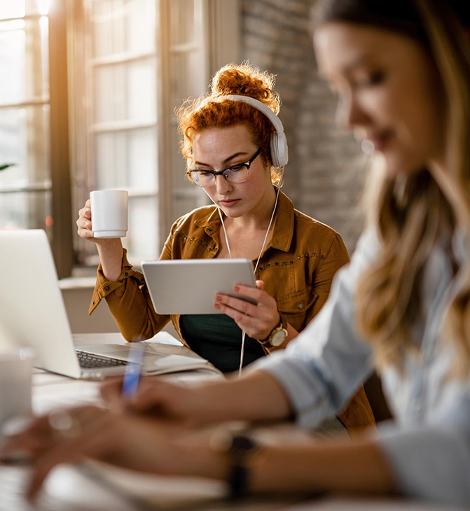Woman sitting in front of a MacBook looking at an iPad