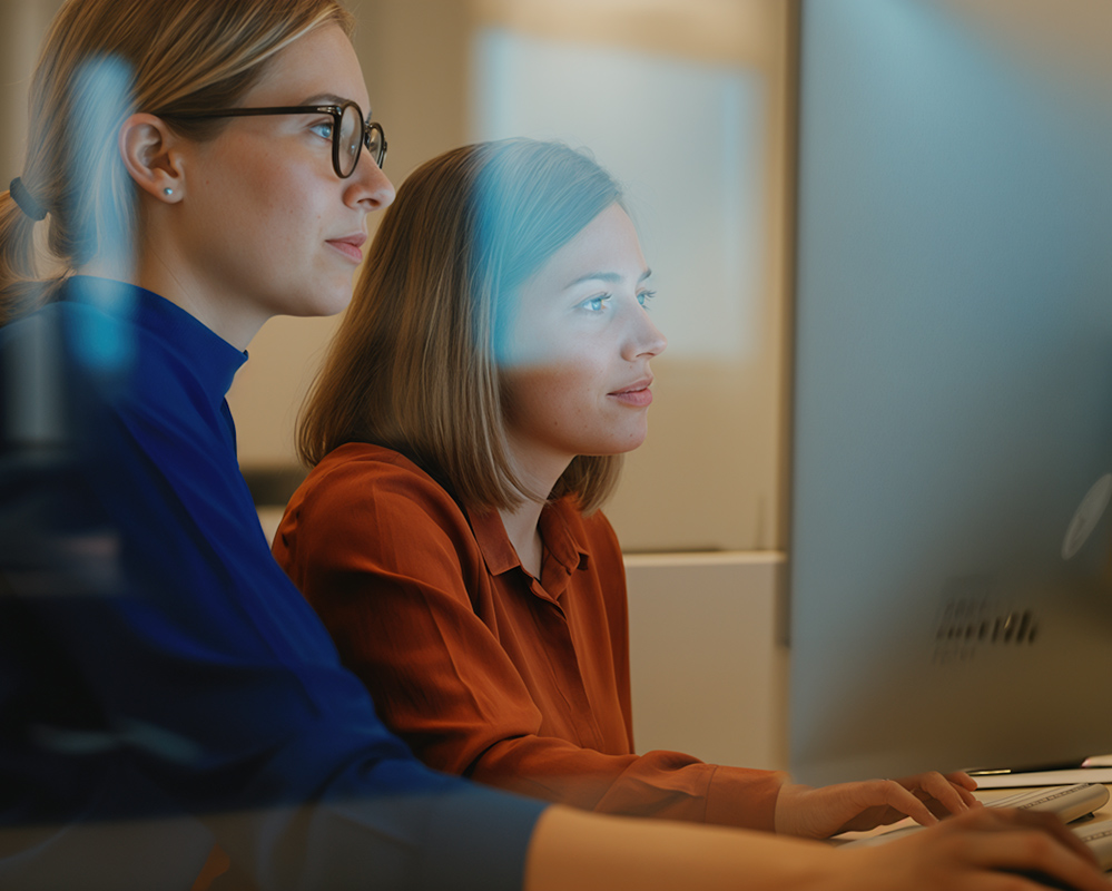 Two women woking side by side on their Mac computers